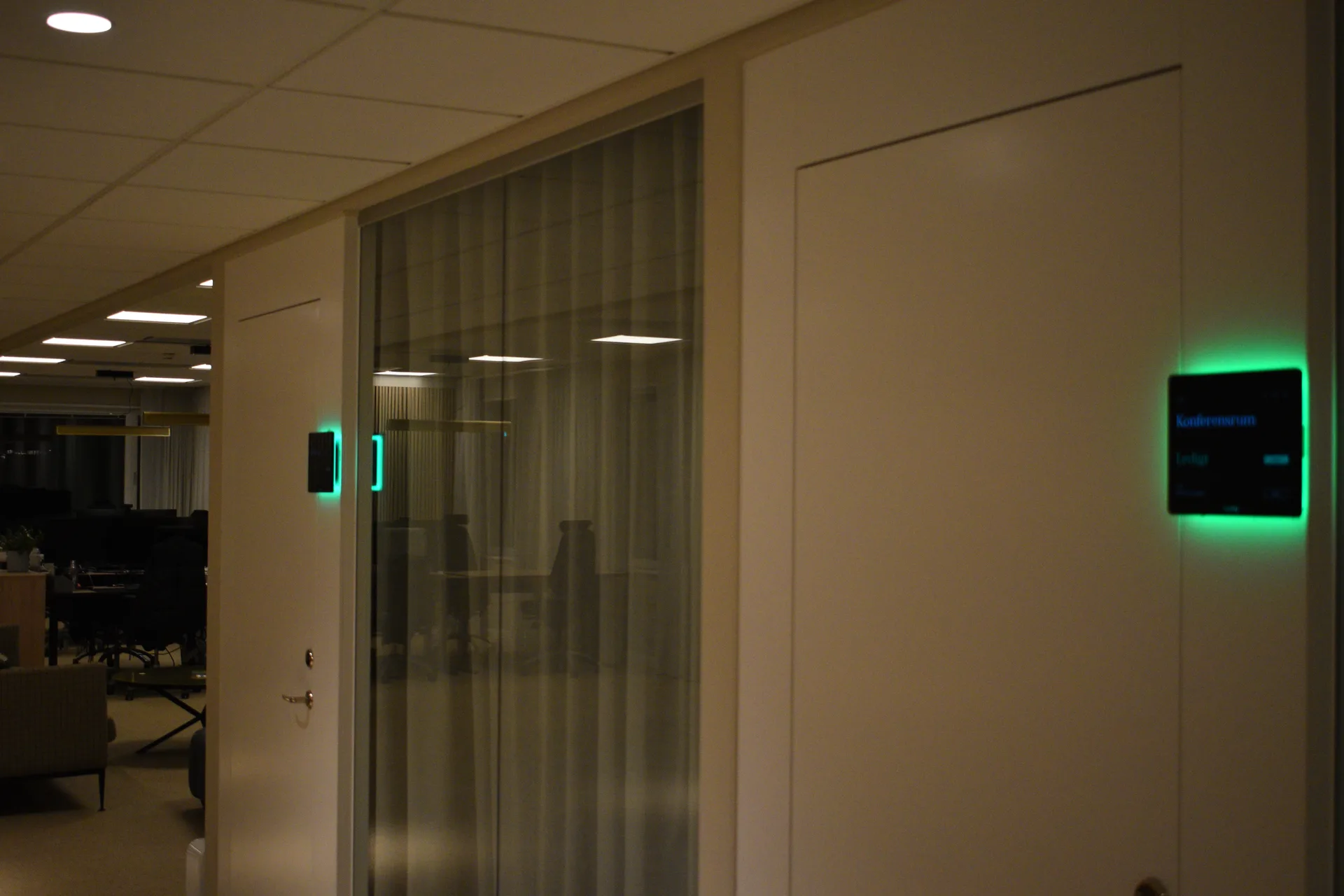 Två Humly-paneler med grönt ljus vid kontorets glasväggar och mötesrum
